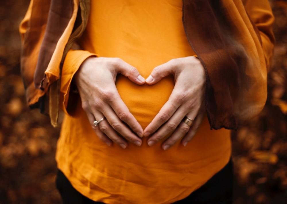 a pregnant woman holding her hands in a heart shape over her belly