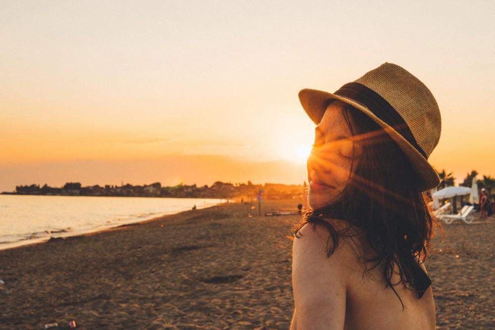 woman in a fedora smiling at sunset on the beach