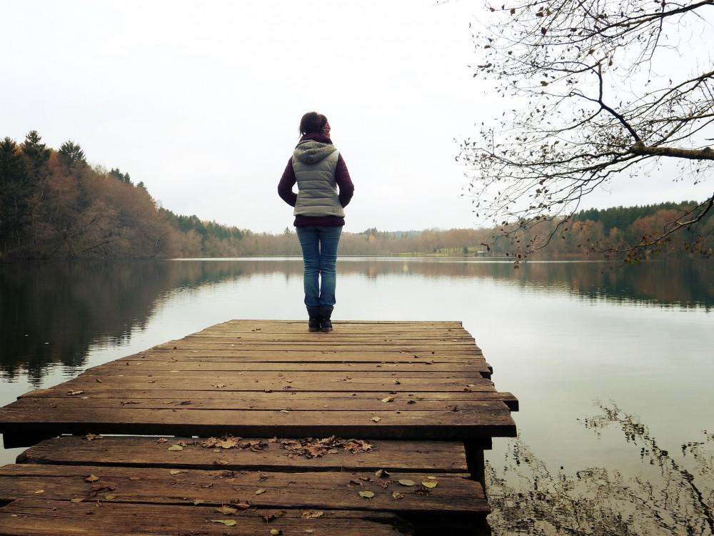 woman standing on the dock of a serene lake