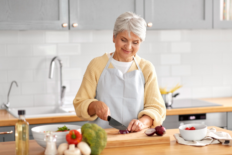 Happy smiling senior woman with knife chopping red onion on kitchen at home